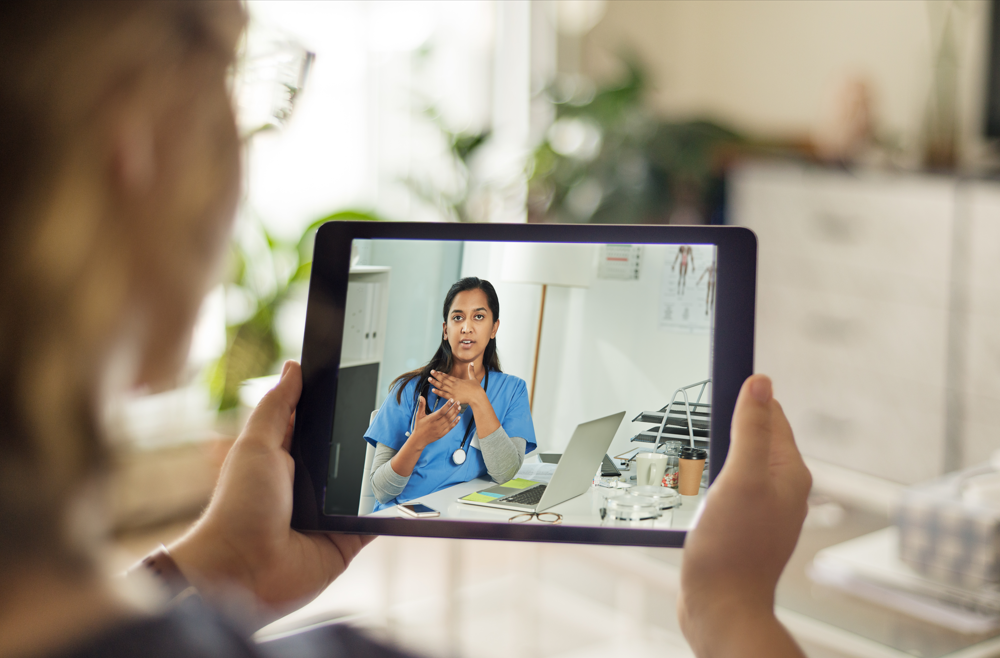 A woman holding an iPad and speaking with a physician on a telemedicine appointment